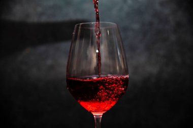 Glass of red wine in half on a dark background.