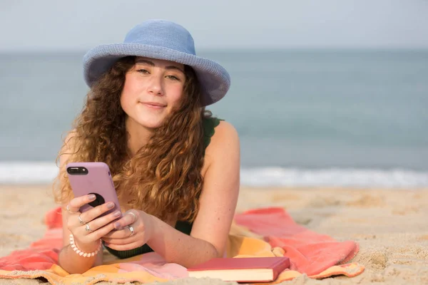 在海滩上拿着毛巾拿着手机的年轻女子 — 图库照片