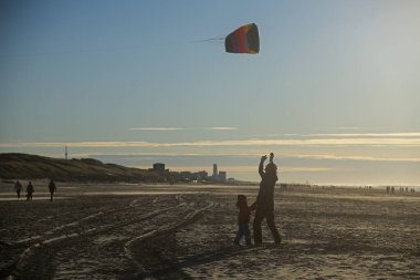Baba ve oğul kış güneşinde kumsalda uçurtma uçuruyorlar.