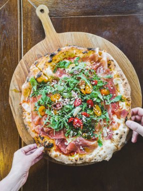 Erkek ve kadın eli ahşap tezgahtan taze bir pizza alır.