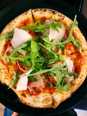 Dört parçaya bölünmüş taze parmesanlı ve roka aromalı bir pizzanın üst görüntüsü.