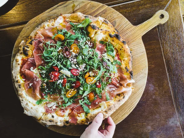 Bir adamın eli, jambonlu, domatesli ve sert etli bir dilim taze pizza alır..