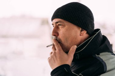 Soğuk bir günde dışarıda sigara içen orta yaşlı bir adam.