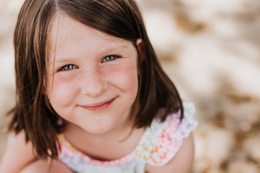 Parlak mavi gözlü, çilli, gülümseyen kız kameraya bakıyor.