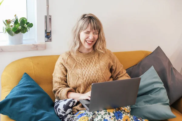 ノートパソコンを持った黄色いソファに座って笑っている若い女性 — ストック写真