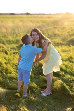 Anne ve oğlu gün batımında tarlada yürür, çocuk annesini öper.