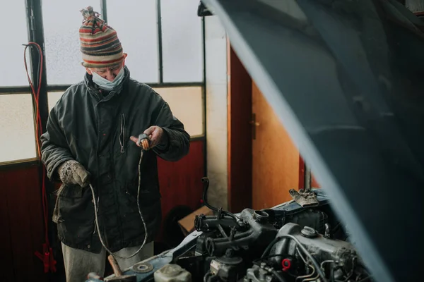 ガレージで保護マスクを持つ老人は彼の古い車を修復します — ストック写真