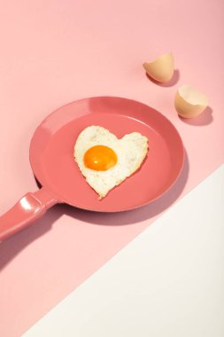 Pembe tavalı ve kalbi beyaz ve pembe arka planda olan yaratıcı bir fikir. En az yemek ve aşk konsepti. Sevgililer Günü için kahvaltı fikri ve romantik bir sabah. Dikey fotoğraf