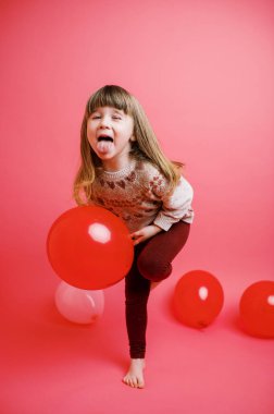 Küçük kız flamingo pembesi üzerinde pembe ve kırmızı balonlarla oynuyor