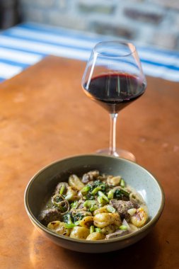 Bir kase kırmızı şarapla servis edilen biftekli gnocchi.