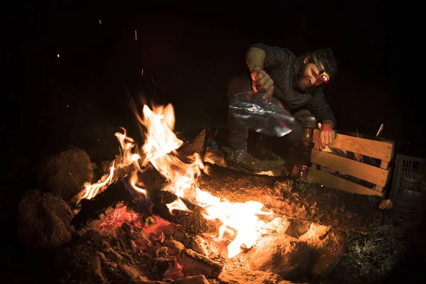 A man blows the campfire to keep it burning