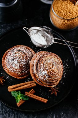 Siyah arka planda tarçınlı çörekler. kahve, şeker, dut