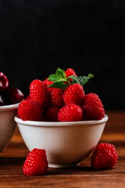Ahşap arka planda bir kasede çeşitli yabanmersini çeşitleri. Ahududu, yaban mersini, kiraz