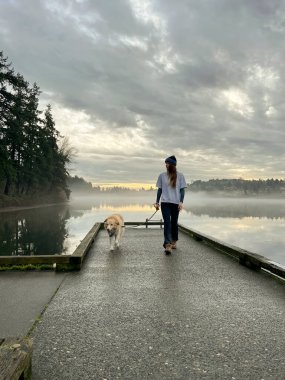 Kadın ve köpekleri Seattle 'daki Seward Park' ta rıhtımda yürüyorlar.
