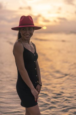 Gün batımında plajda gülümseyen kırmızı şapkalı hoş Latin kız.