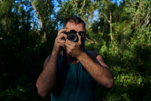 Genç adam klasik kamerayla doğada fotoğraf çekiyor.