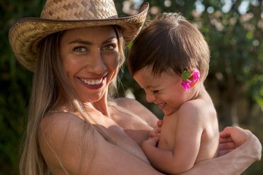 Genç Latin anne oğlunu taşıyor ve güneşli bir öğleden sonra gülümsüyor.