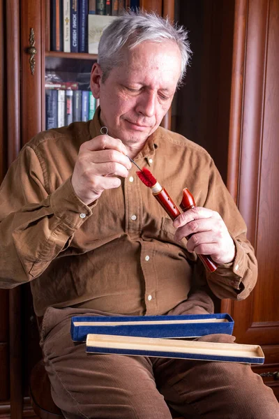 Elderly Man Cleans Wooden Flute While Sitting Chair — Stock Photo, Image