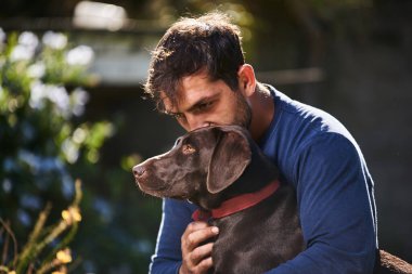 Genç adam köpeğine sarılıyor.