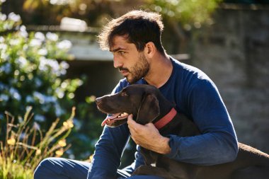 Genç adam köpeğine sarılıyor.