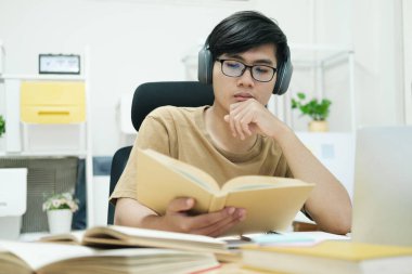 Genç erkek öğrenci evde ders çalışıyor. Bilgisayarı kullanıyor ve internetten öğreniyor.