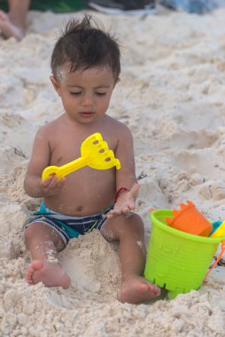 Latin çocuk, Karayip sahilinde oyuncaklarla kumsalda oynuyor.