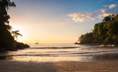 Kosta Rika 'da gün batımında okyanusta insanların olduğu plaj sahnesi..