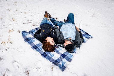 Karla çevrili mavi bir battaniyenin üzerinde yatan adam ve kadın.