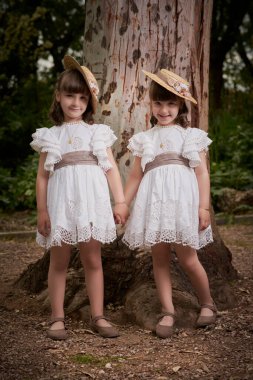 Komünyon ikizleri parkta büyük bir ağacın yanında.