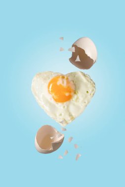 kalp şeklinde çırpılmış yumurta ve yumurta kabuğu mavi arka planda uçuyor.