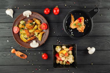 Mantarlı kızarmış patates ve baharatlı siyah ahşap arka planda domates. Sebzeli patates ve siyah tavada kızarmış tavuk. Sebze ve patatesli kızarmış tavuk..