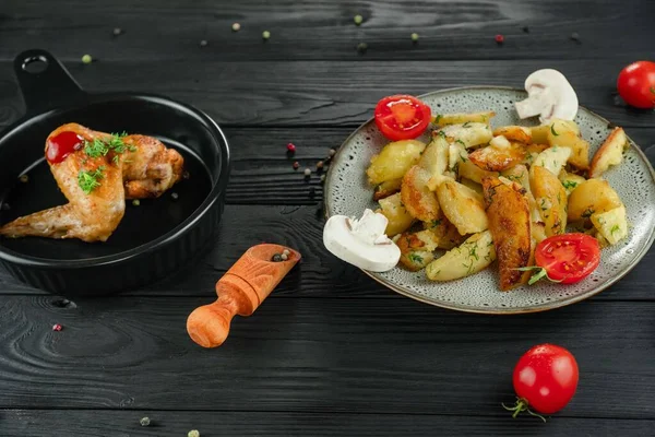 Mantarlı kızarmış patates ve baharatlı siyah ahşap arka planda domates. Sebzeli patates ve siyah tavada kızarmış tavuk. Sebze ve patatesli kızarmış tavuk..