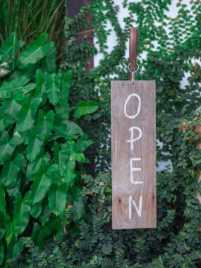 Yeşil yaprakların arkaplanındaki açık tabela resmi. Arka planda yeşil yapraklar olan demir bir direğe asılı açık tabela. Küçük işletmeler için tabela