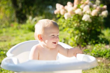 Sarışın çocuk bir yaz günü yeşil çimenlikte bebek banyosunda gülümser.