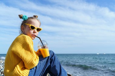 Kız sahilde oturmuş meyve suyu içiyor..