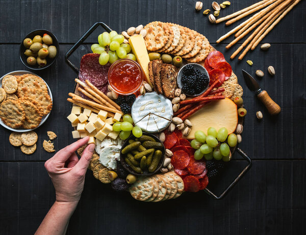Hand over charcuterie board of meat, cheese, fruit, crackers.