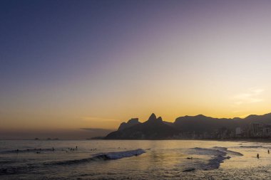 Ipanema, Rio de Janeiro, Brezilya 'da okyanus, dağlar ve turuncu gökyüzü ile güzel sahil gün batımı manzarası