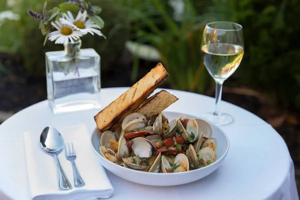 A clam and pasta dish with wine in outdoor setting