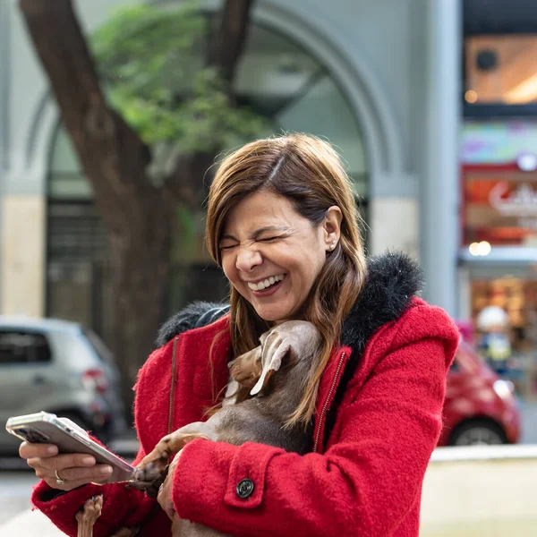 Latynoska Kobieta Używa Smartfona Śmieje Się Trzymając Psa — Zdjęcie stockowe