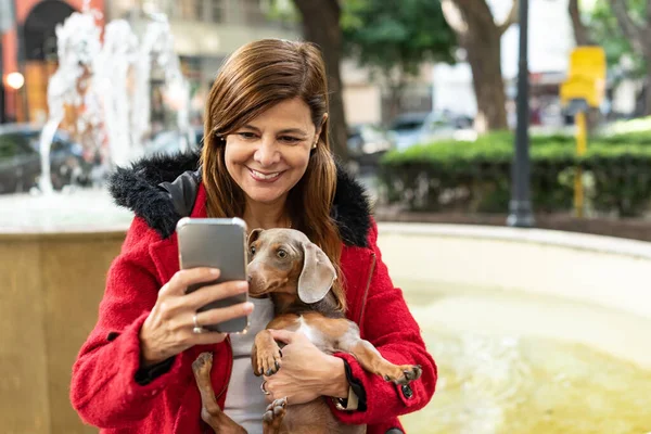 Латинская Женщина Проверяет Сообщения Своем Смартфоне Держа Свою Собаку — стоковое фото