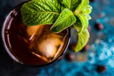 Köpüklü Kremşantili Beyaz Rus kokteyli bardakta servis edilir ve kahve çekirdekleri ve taze nane yapraklarıyla süslenir.