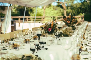 Mumlar, çiçekler ve masa koşucusuyla dolu uzun bir masa. Düğün masası.