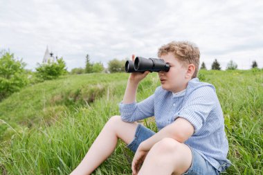 An 11-year-old boy on a walk, look through binoculars.