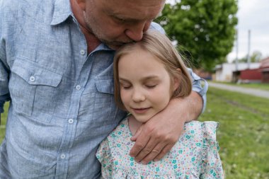 Baba kızının başını nazikçe öpüyor ve ona sarılıyor..