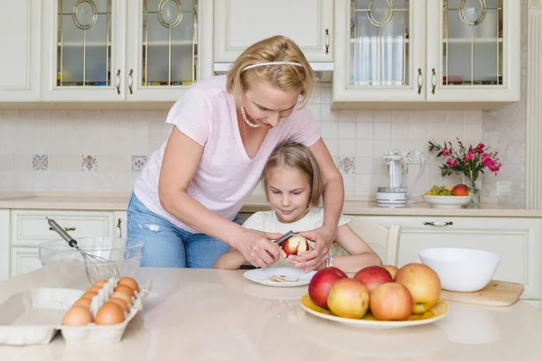 Mom helps her daughter in the kitchen, teaches her to peel  an apple.