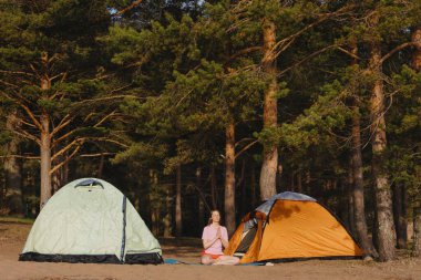 Lotus pozisyonunda bir kadın ve ormandaki çadırların arasında namaste.
