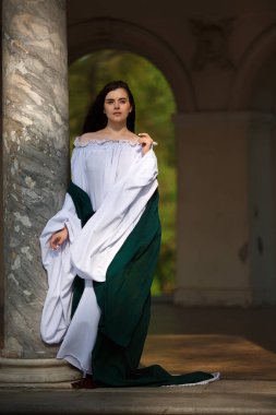 Beautiful young woman in white-green medieval clothes looks ahead