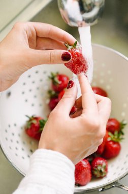 Mutfakta çilek yıkayan bir kadının yakın çekimi.