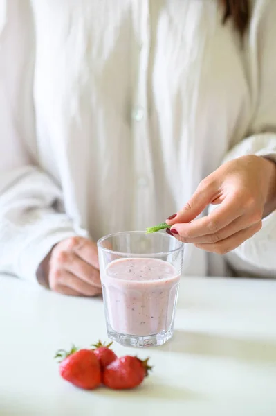 woman decorating a strawberry smoothie with green peppermint