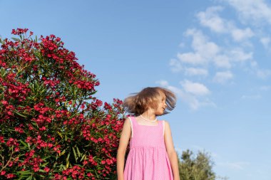 Çiçekli zakkum çalılarının yanında bir kızın portresi.